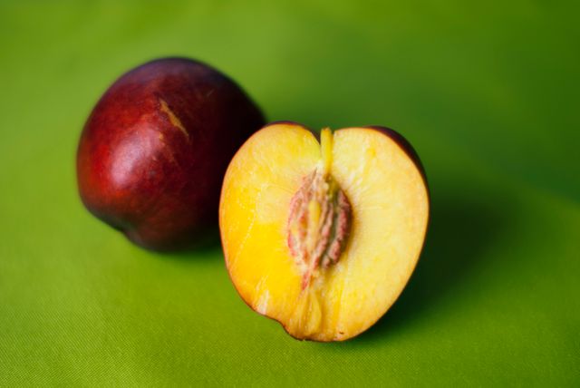 Fresh nectarine with one half revealing the juicy interior against a vibrant green background. Perfect for uses in food blogs, recipe illustrations, and health articles promoting nutritious diet tips.