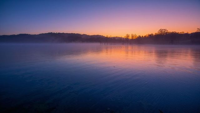 Sunrise Mist Reflecting Over Tranquil Lake Mirror Surface With Soft Pastel Sky Fog Ripples