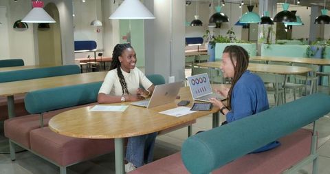 African American Coworkers Discussing Data on Laptops in Modern Coworking Lounge