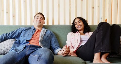 Diverse couple relaxing on sofa, holding hands, enjoying moment