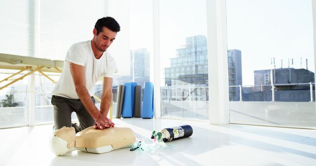 Young man practicing CPR chest compressions on a mannequin in a bright, modern classroom. Great for emphasizing first aid training, emergency response skills, medical education, health class materials, and life-saving techniques across various education and health awareness platforms.