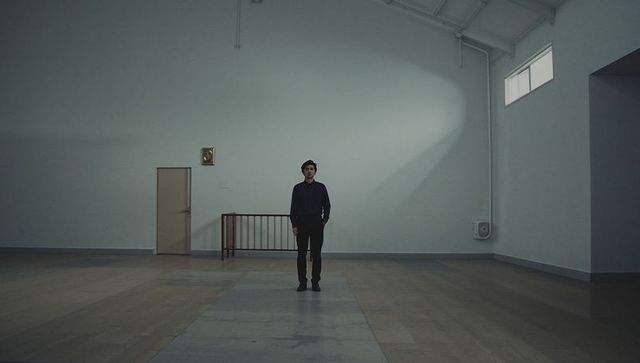 Standing man in vast minimalist vaulted hall with dramatic sunlight beam and wooden runner