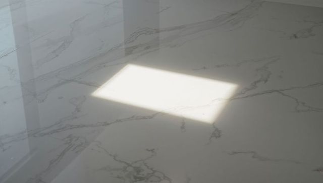 Showing rectangular sunlight patch on polished white marble countertop with window shadow