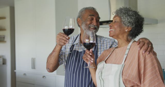 Happy african american senior couple drinking wine together in kitchen. healthy, active retirement lifestyle at home.