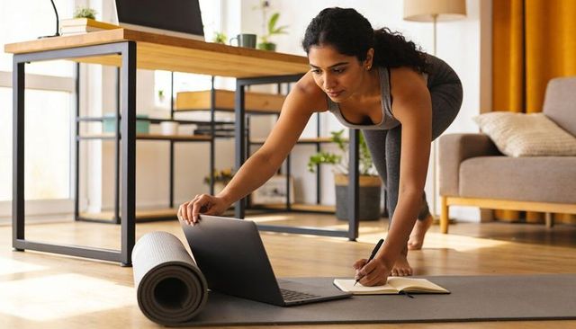 Indian woman practicing plank and taking notes during guided online yoga workout