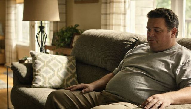 Resting man sitting on sofa in cozy living room with soft daylight and reading lamp