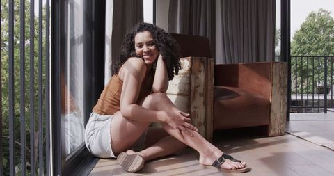 Sunlit apartment portrait: african american woman sitting by balcony door smiling