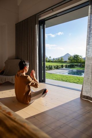 Young person meditating indoors by open sliding door with pool and mountain view