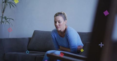 Woman suffering abdominal discomfort on modern gray sofa in contemporary home
