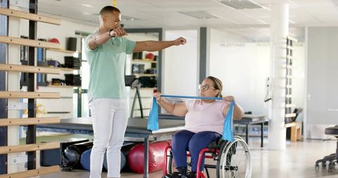 Therapist Guiding Wheelchair Patient Pulling Resistance Band During Rehabilitation Session