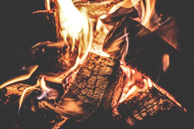 Close-up view of burning wood in a cozy campfire with bright, glowing flames. Ideal for use in camping, outdoor activities, and nature-themed promotions, or as a background for relaxation and warmth visuals.