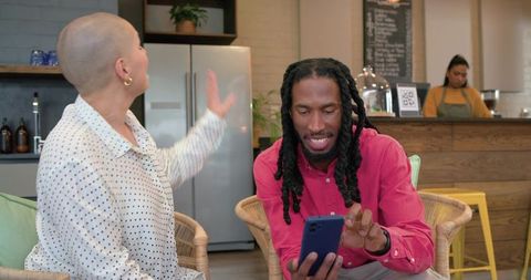 Diverse friends sharing laughter while browsing smartphone in cozy urban coffeehouse