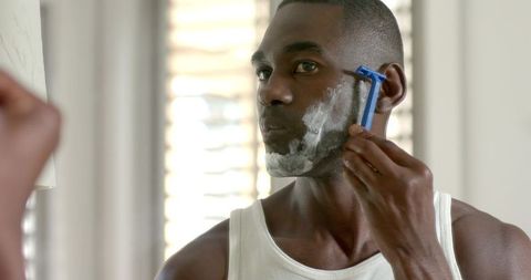 African american man shaving at mirror morning grooming routine in home bathroom