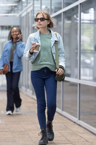 Young woman walking with coffee and sunglasses through modern glass pedestrian corridor