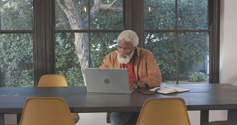 Focused senior man writing in notebook next to laptop