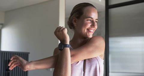 Woman stretching arm after workout wearing smartwatch in modern minimalist room