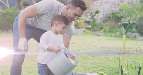 Father teaching son gardening and watering flowers in sunny backyard with watering can
