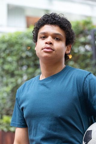 Young african man standing holding soccer ball in urban courtyard wearing teal t-shirt