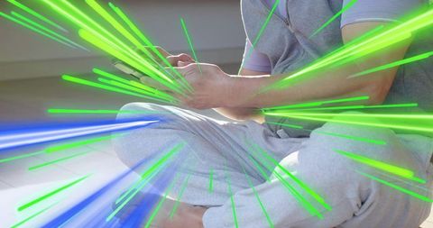 Asian man sitting cross-legged tapping smartphone with neon green and blue streaks overlay