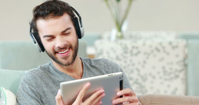 Young man enjoying music while using a tablet. Perfect for illustrating concepts like modern living, relaxation, technology use, and digital lifestyles.