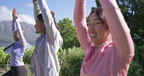 Multicultural friends stretching in sunlit garden with mountain view