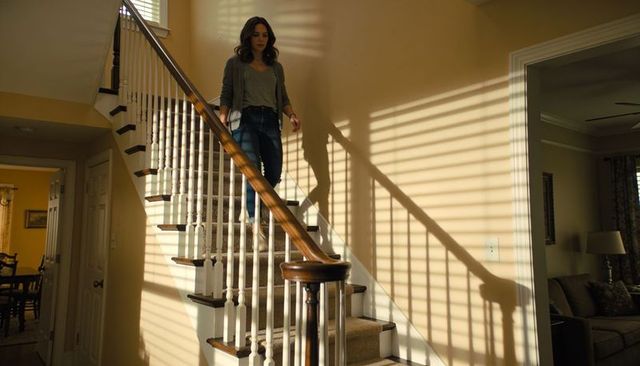 Woman descending carpeted staircase in sunlit home with blinds casting shadow stripes