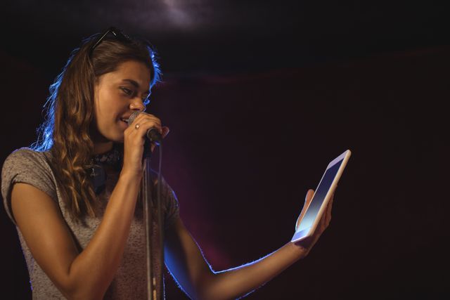 Confident female singer holding digital tablet while performing at music concert