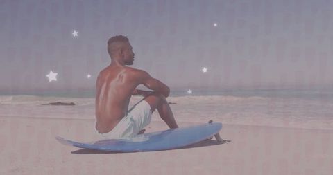 Shirtless man relaxing on surfboard by ocean shoreline under clear sky