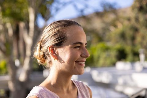 Young woman smiling in golden sunlight on terrace wearing sleeveless top and gold hoops