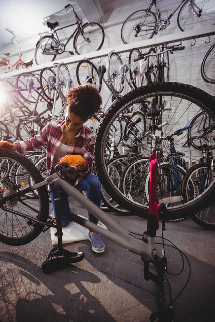 Woman mechanic repairing a bicycle in a bike workshop. Surrounded by various bicycles, she is focused on fixing a bike using tools. Ideal for use in subjects concerning bike maintenance, mechanic work, cycle shops, and promoting women in trades.