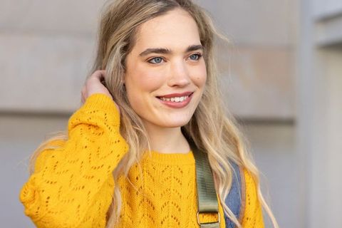 Young woman smiling wearing mustard knit sweater with olive backpack strap urban portrait