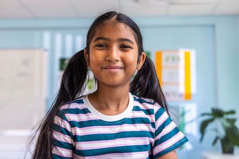 Smiling elementary schoolgirl with pigtails in bright modern classroom, education portrait