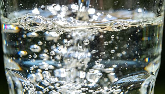 Macro pouring water creating sparkling air bubbles and prism refraction in clear glass