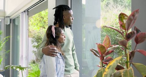African American Man and Indian Woman Embracing by Sliding Glass Doors Standing with Indoor Plants