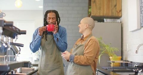 Baristas tasting espresso and laughing behind counter in modern specialty cafe