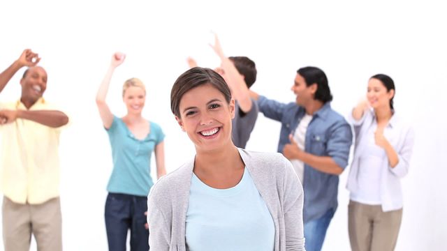 A cheerful woman smiles in the foreground while friends dance energetically in the background. This scene embodies happiness, positivity, and a sense of camaraderie. Ideal for promotional materials encouraging teamwork, joyful events, or positivity-focused campaigns.