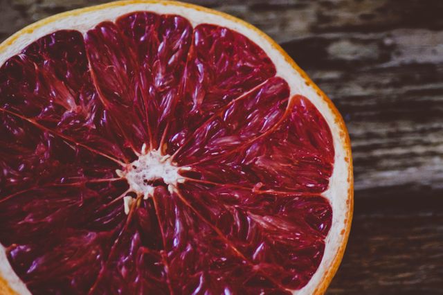 Close-up of a blood orange showing its vibrant red interior against a dark wooden surface. Ideal for use in health and nutrition blogs, cooking websites, or as illustrative content for articles about fresh produce and healthy living.