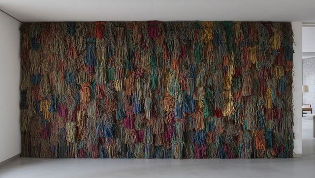 Large multicolor yarn tassel wall installation showcasing textured fiber art in gallery