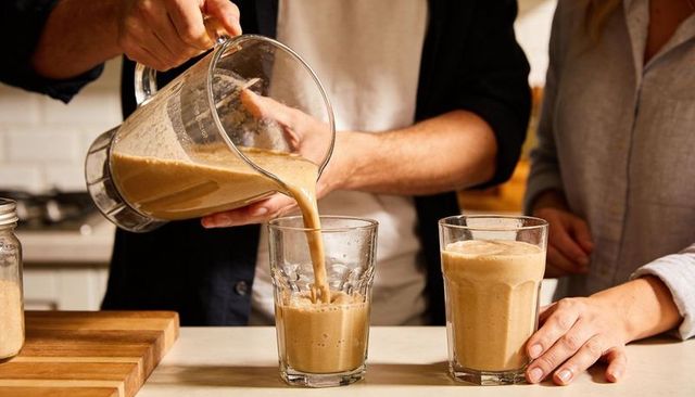 Couple pouring creamy nutritious smoothie in home kitchen, casual morning routine