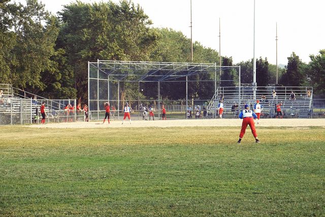 Image shows youth baseball players engaging in a game on a sunny summer day. Perfect for use in projects related to youth sports, community activities, team spirit, recreational leagues, and family outings. Ideal for advertising sports equipment, youth leagues, and sporting events.