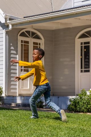 African american boy running on lawn in yellow shirt by front porch with arched doors