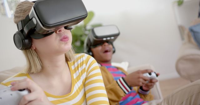 Two friends are having fun with virtual reality gaming in a cozy home environment. The girl in the foreground is fully immersed in the experience, while her male friend in the background seems excited. Ideal for use in articles, blogs, or advertisements focusing on virtual reality, gaming trends, technology, or teenage leisure activities.