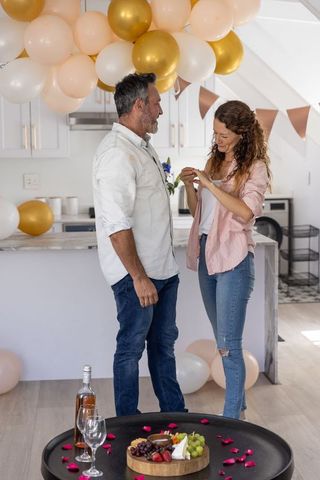 Mature couple celebrating in modern kitchen with balloons, rose wine and charcuterie board