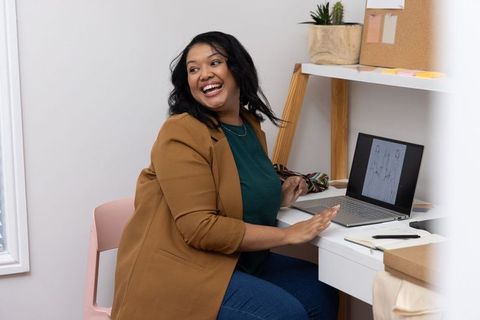 African american freelance designer laughing while working at home desk with laptop sketches