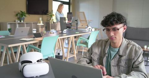 Young professional typing on laptop in modern coworking space with vr headset on table