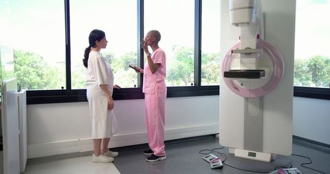 African American technologist consulting patient in gown before mammogram with modern unit