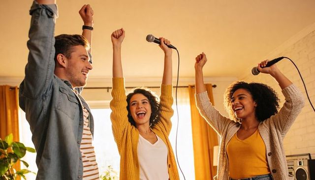 Friends singing karaoke at home celebrating joyful night with microphones and warm light