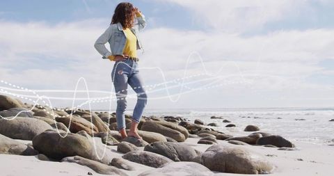 Woman in denim exploring rocky beach in sunlight