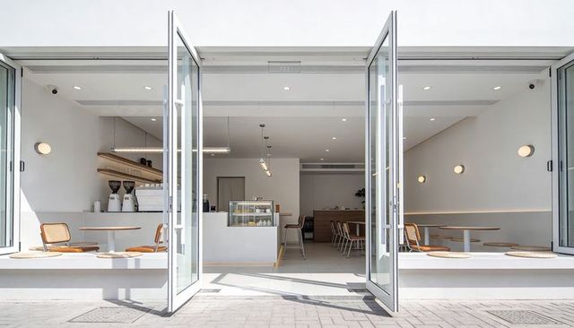 Opening bright minimalist cafe featuring glass bifold doors, pastry display and espresso bar