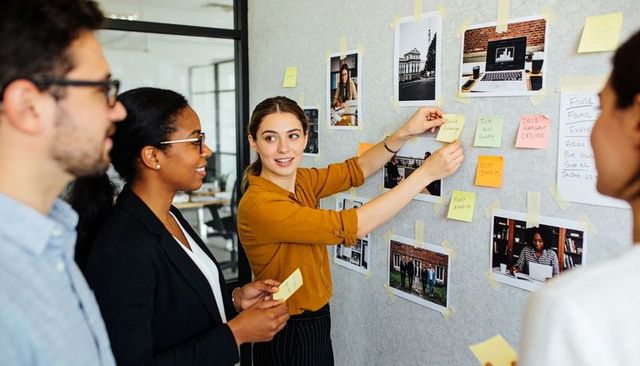Team brainstorming on pinboard with sticky notes and photos in modern open-plan office